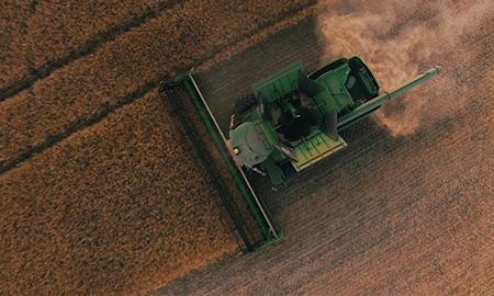 Combine harvester cutting crops in a large agricultural field from aerial view - widenerins.com