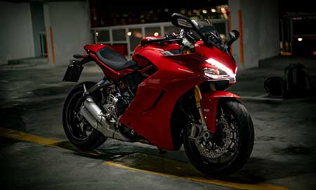 A sleek red motorcycle is parked in a dimly lit garage - https://www.widenerins.com/