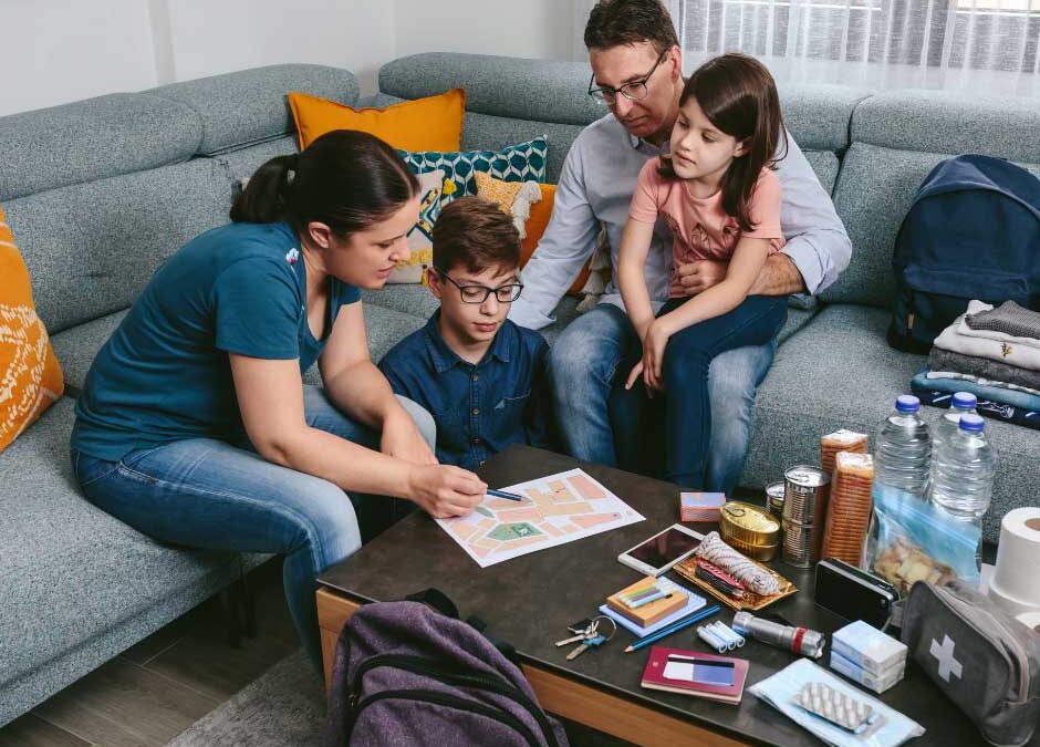 A family of four sits together on a couch surrounded by their belongings, smiling and enjoying each other's company